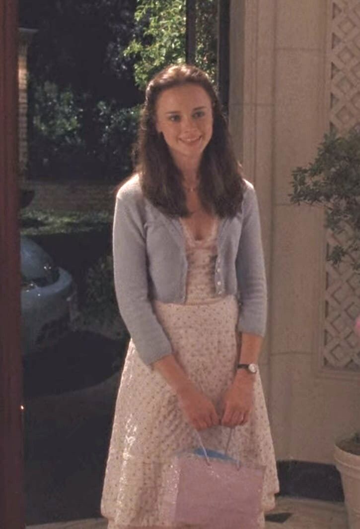 a woman in a dress and cardigan holding a pink bag