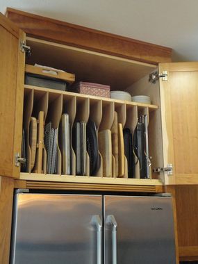 a kitchen cabinet filled with lots of plates and cups in it's drawer next to a refrigerator