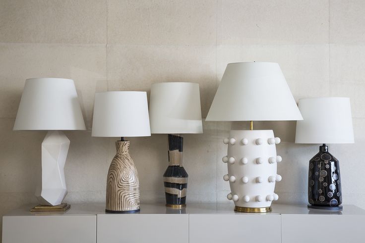 five lamps are lined up on a white shelf with two vases and one lamp