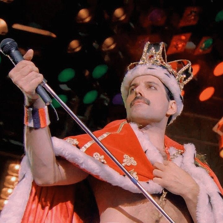 a man dressed in an orange and white costume holding a microphone while wearing a crown