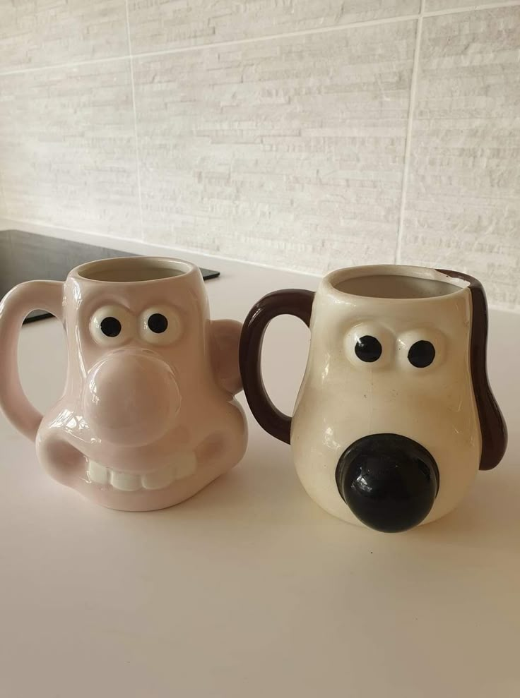 two coffee mugs with faces on them sitting next to each other