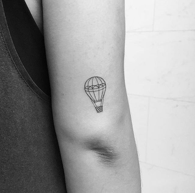 a small hot air balloon tattoo on the left inner arm, with a black outline