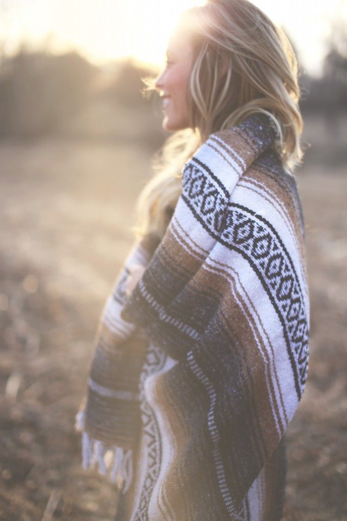 a woman standing in the middle of a field wearing a ponchy and sweater