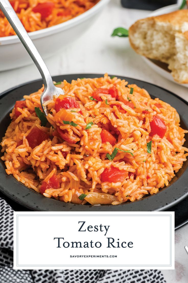 a black plate topped with tomato rice next to a bowl of bread and a fork