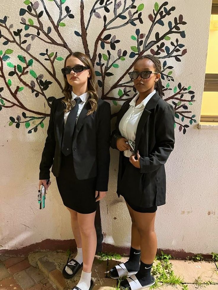 two women dressed in school uniforms standing next to a tree with leaves painted on it