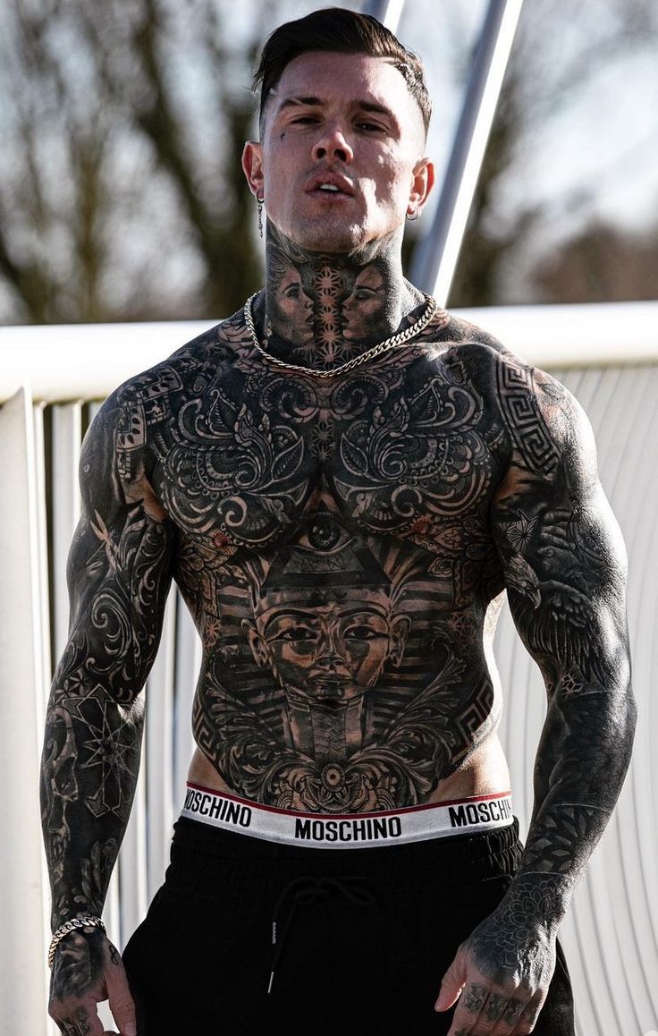 a man with tattoos on his chest standing in front of a white fence and looking off into the distance