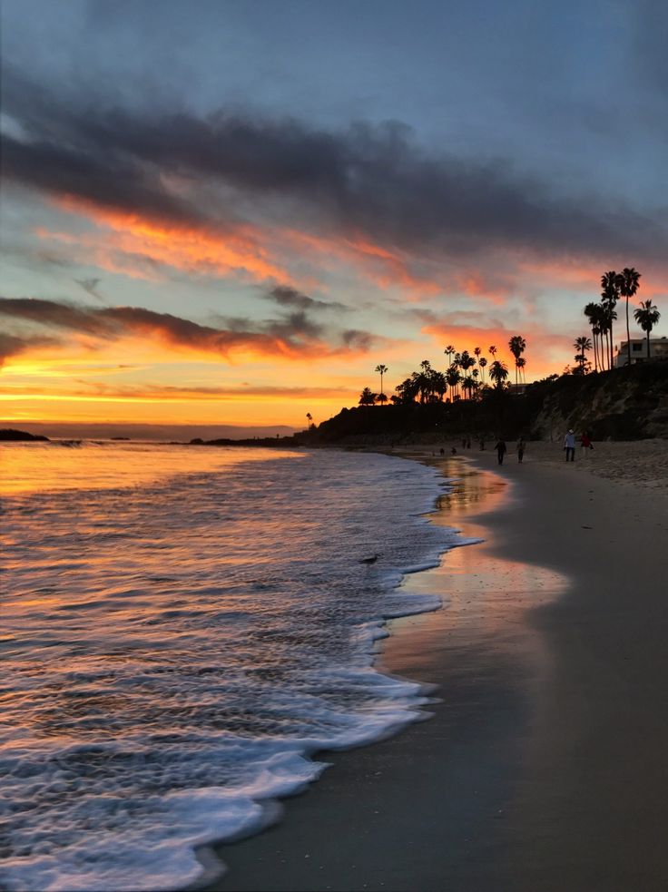 people are walking along the beach at sunset