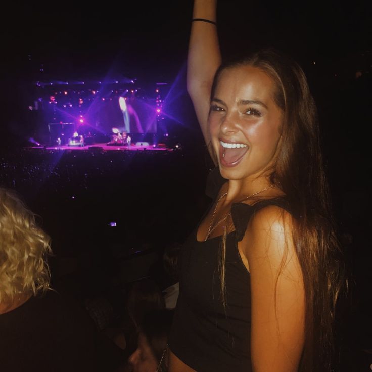 a beautiful young woman standing in front of a stage holding her arm up to the sky