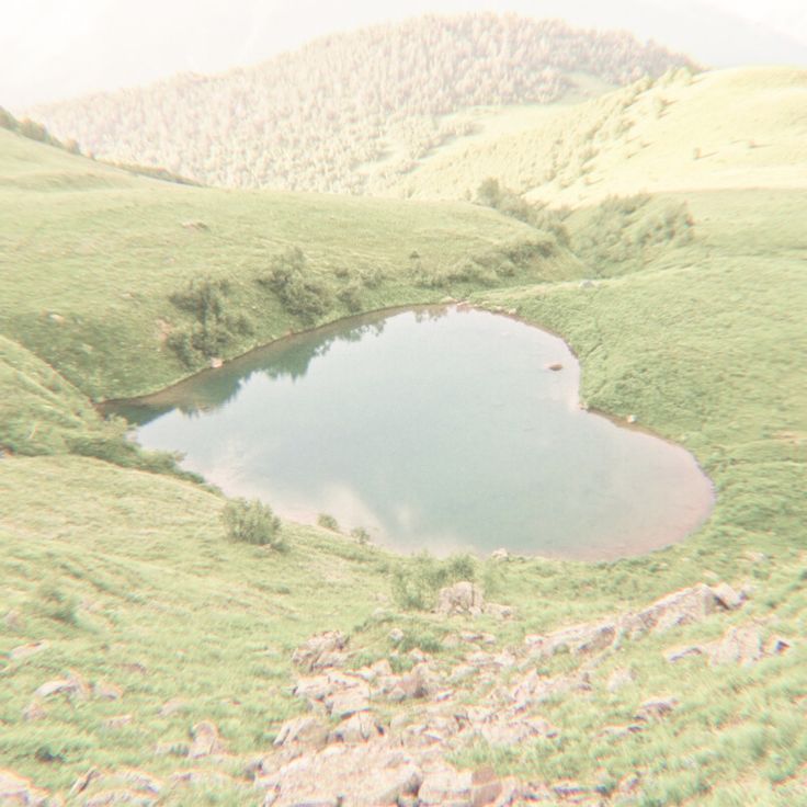 there is a small pond in the middle of this mountain range with grass and rocks around it