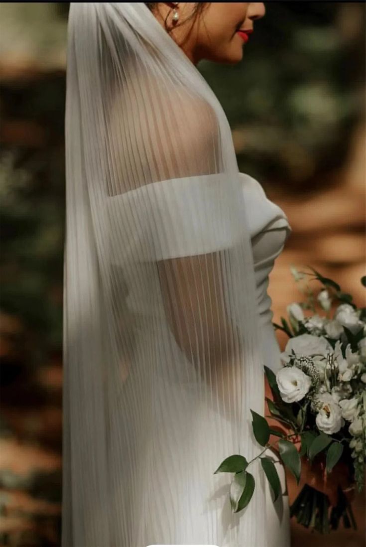 a woman in a white dress holding a bouquet and wearing a veil with flowers on it