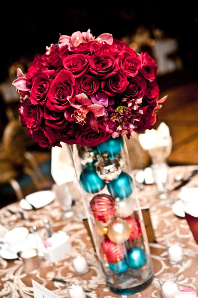 a vase filled with red roses sitting on top of a table next to candles and plates