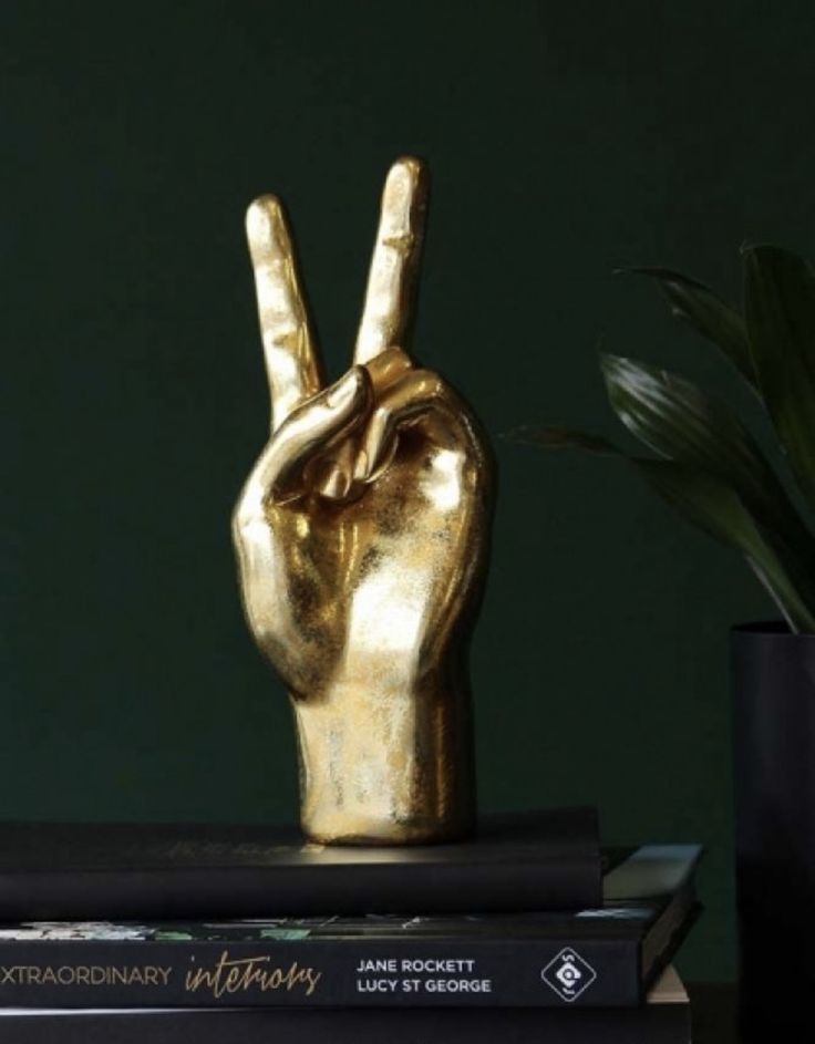 a gold hand statue sitting on top of two books next to a potted plant