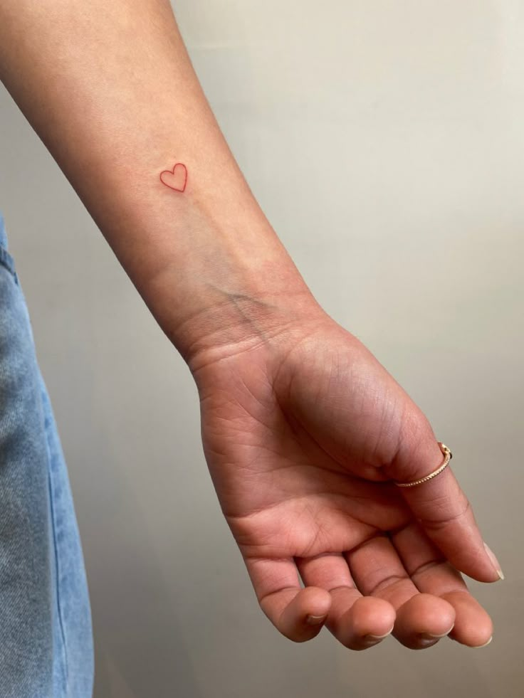 a woman's arm with a small red heart tattoo on the left wrist and right hand