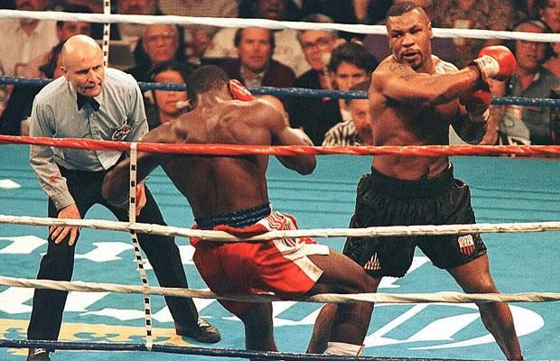 two men in boxing ring with referee and crowd watching from the sidelines looking on