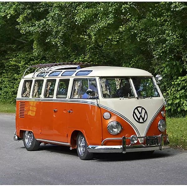 an orange and white vw bus parked on the side of the road with trees in the background