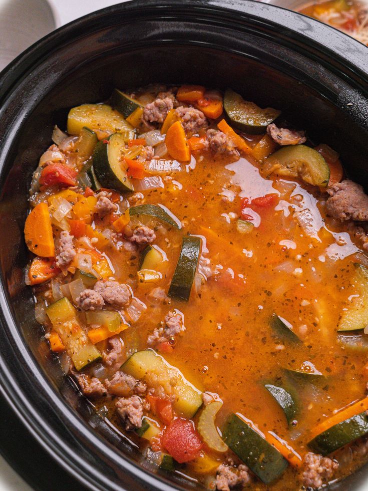 a crock pot filled with meat and vegetables next to some bread on a table