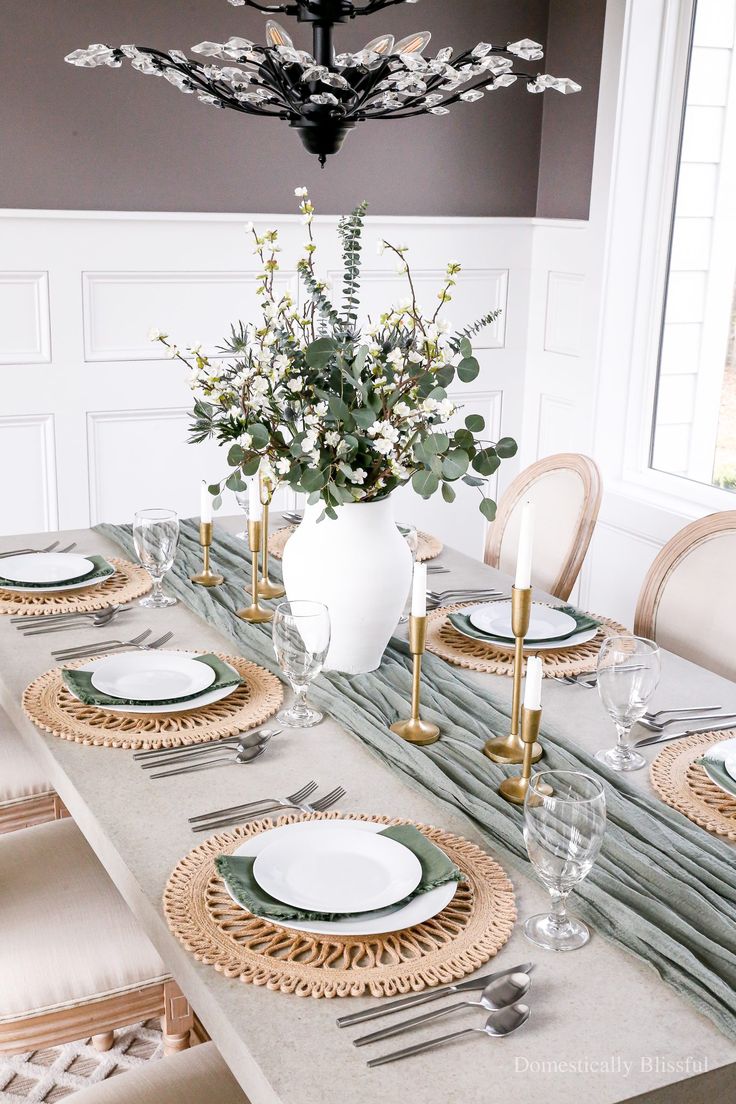 a dining room table set with place settings and flowers in a vase on the centerpiece