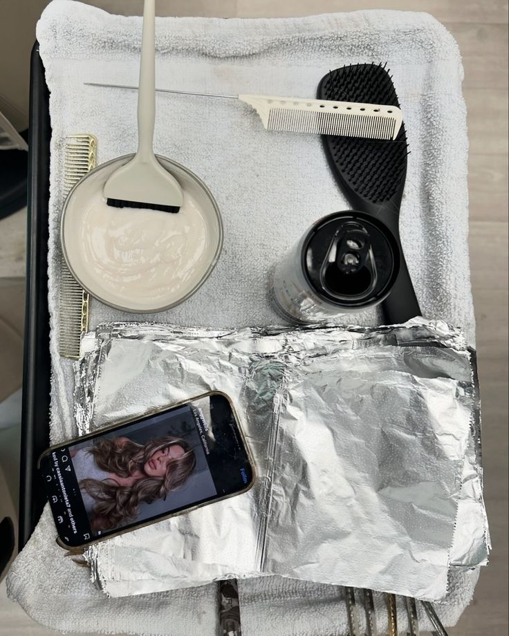 a cell phone sitting on top of a piece of tin foil next to a hair brush