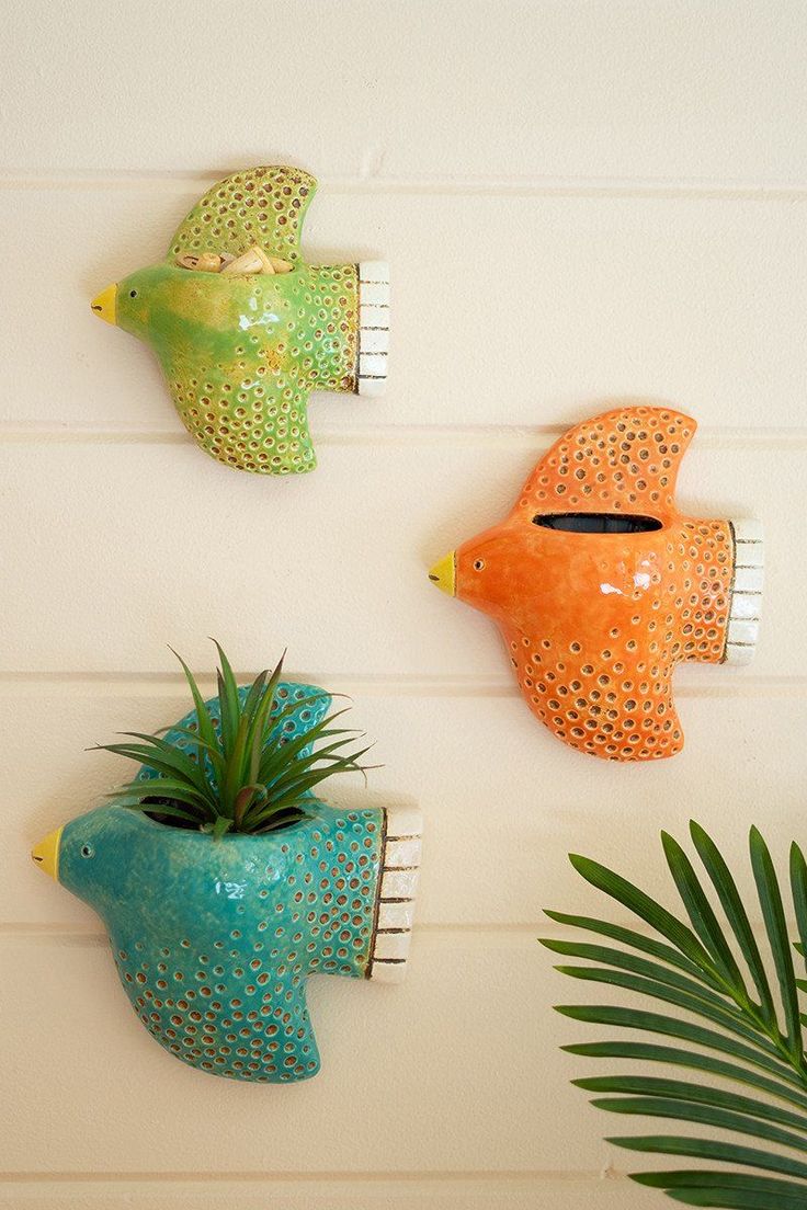 three ceramic fish mounted to the side of a wall next to a potted plant