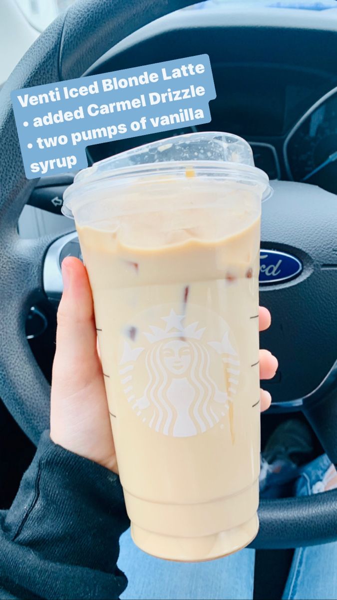 a person holding up a drink in their hand while sitting in a car with the steering wheel behind them