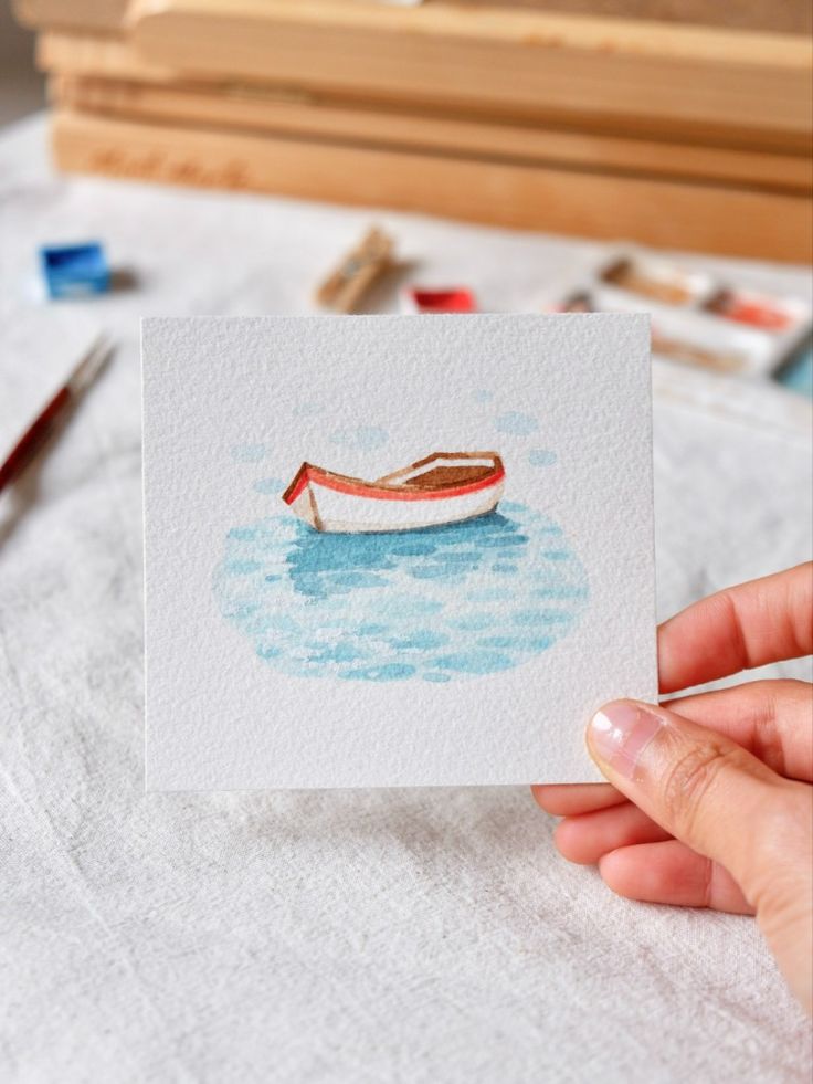 a person holding up a piece of paper with a boat in the water on it