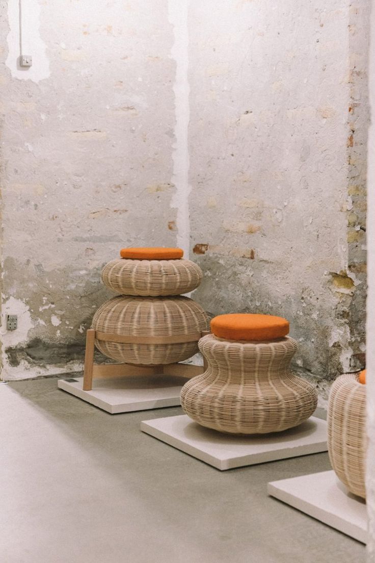 three wooden stools with orange cushions sit in front of a white wall and cement floor