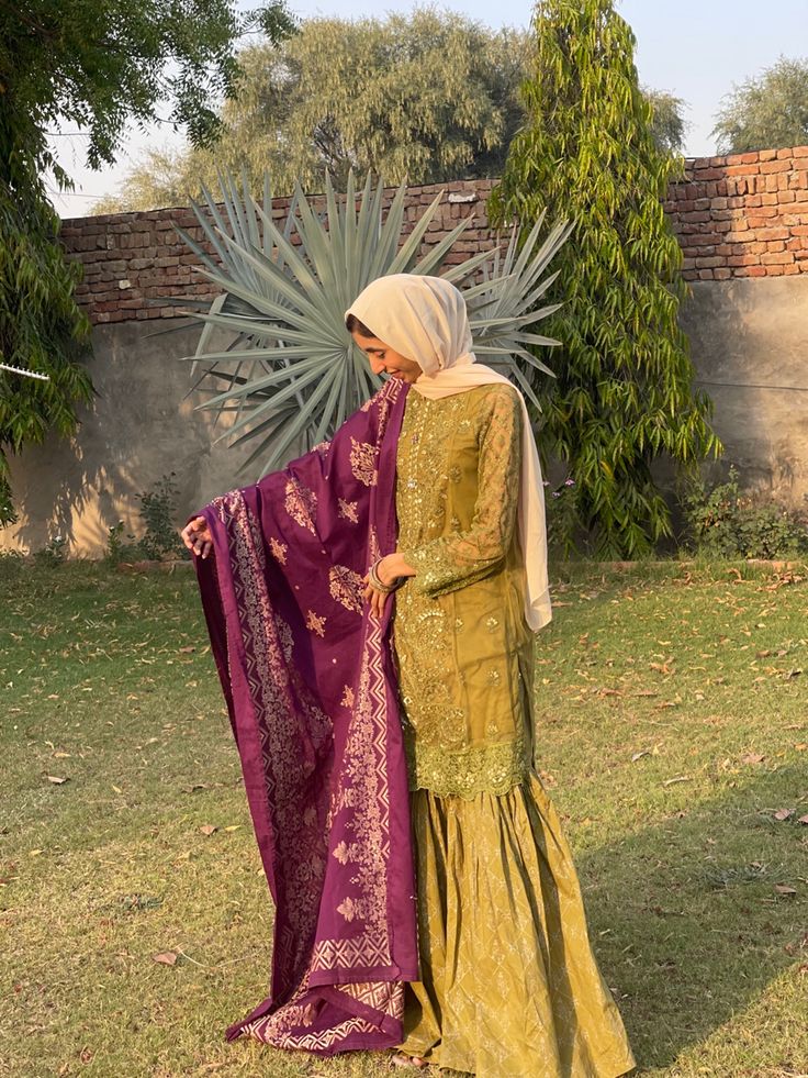 a woman in a yellow and purple dress standing on grass with her back to the camera