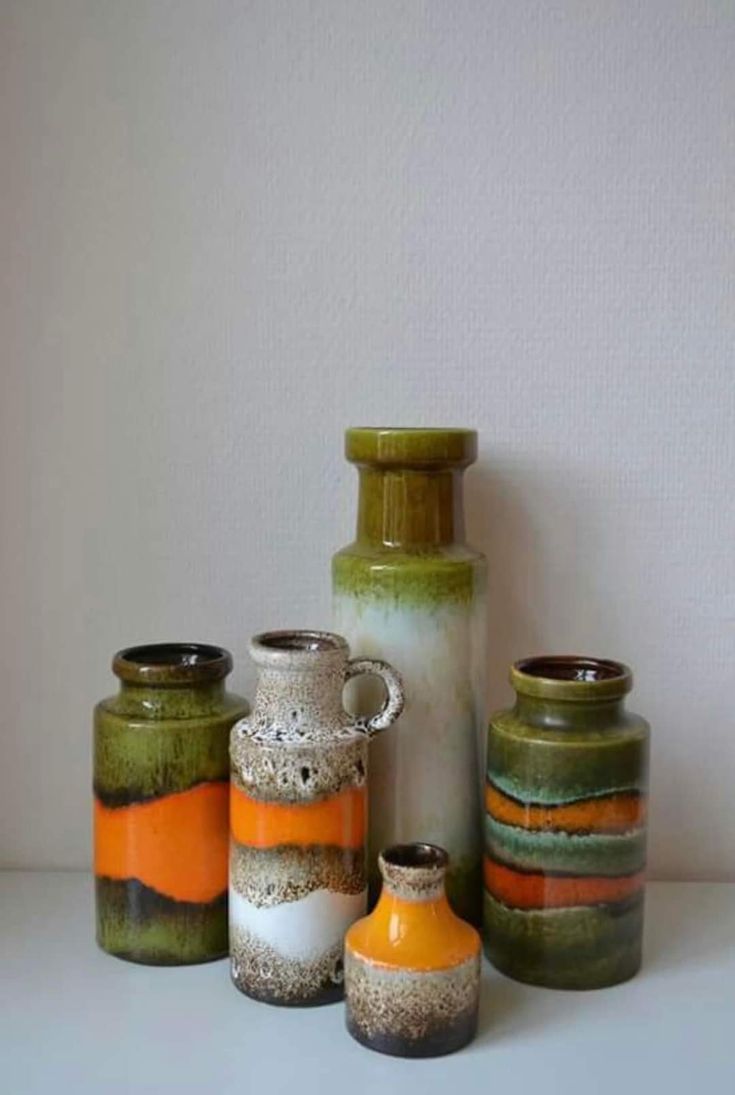 several vases are lined up on a table with white wall in the back ground