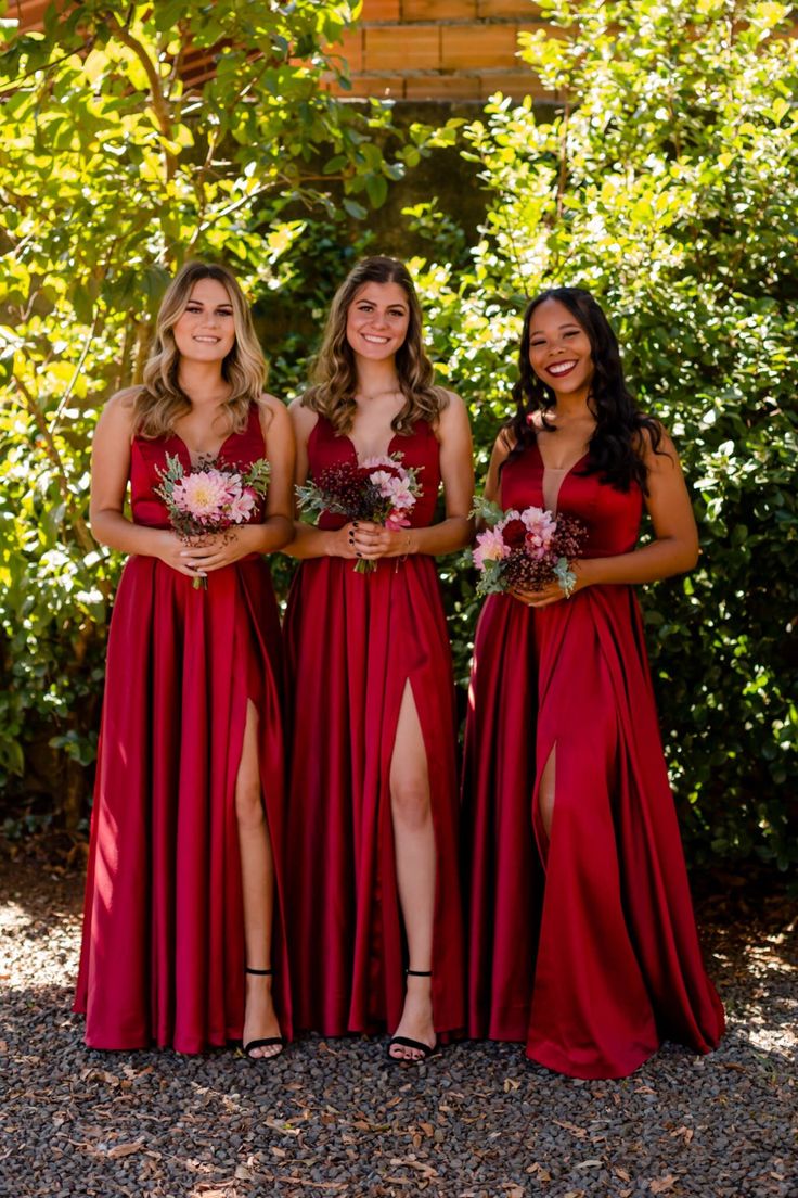 three women in red dresses standing next to each other with their legs split open and holding bouquets