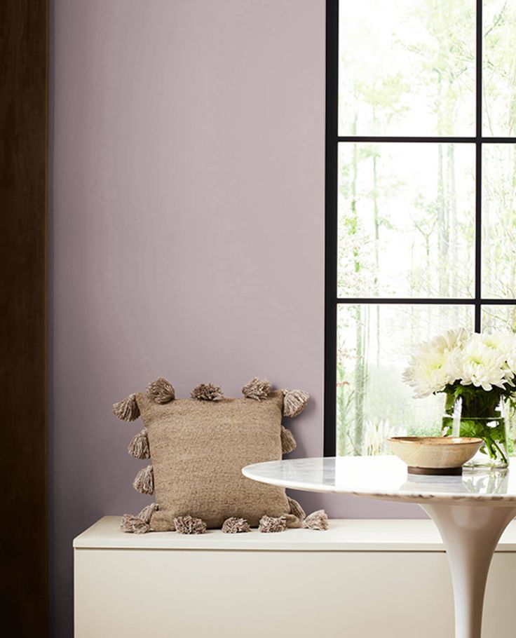 a vase with flowers sitting on top of a white table next to a large window