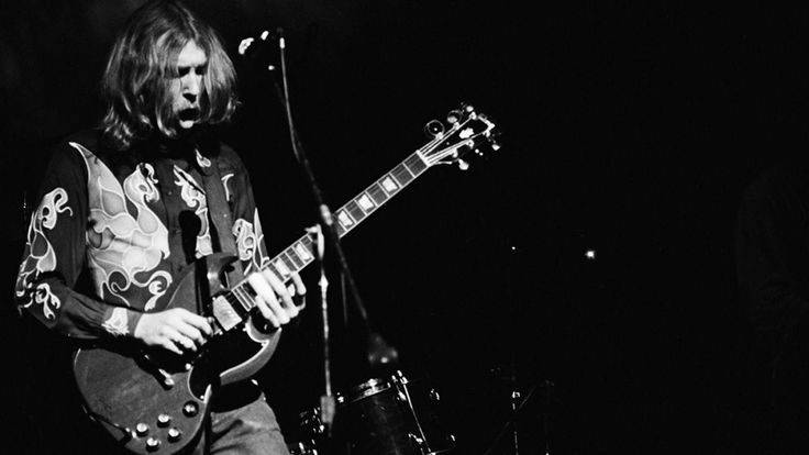 a black and white photo of a man playing an electric guitar in front of a microphone