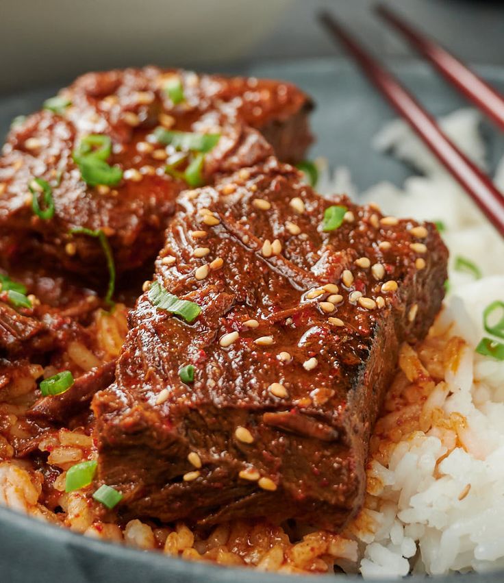 some meat and rice in a bowl with chopsticks on the side for garnish