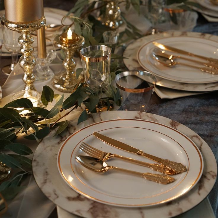 the table is set with white and gold plates, silverware and candlesticks