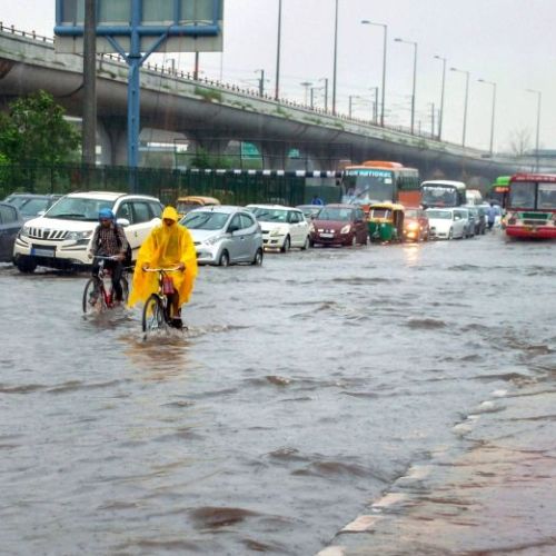 two people in yellow raincoats riding bikes through a flooded street with cars and buses