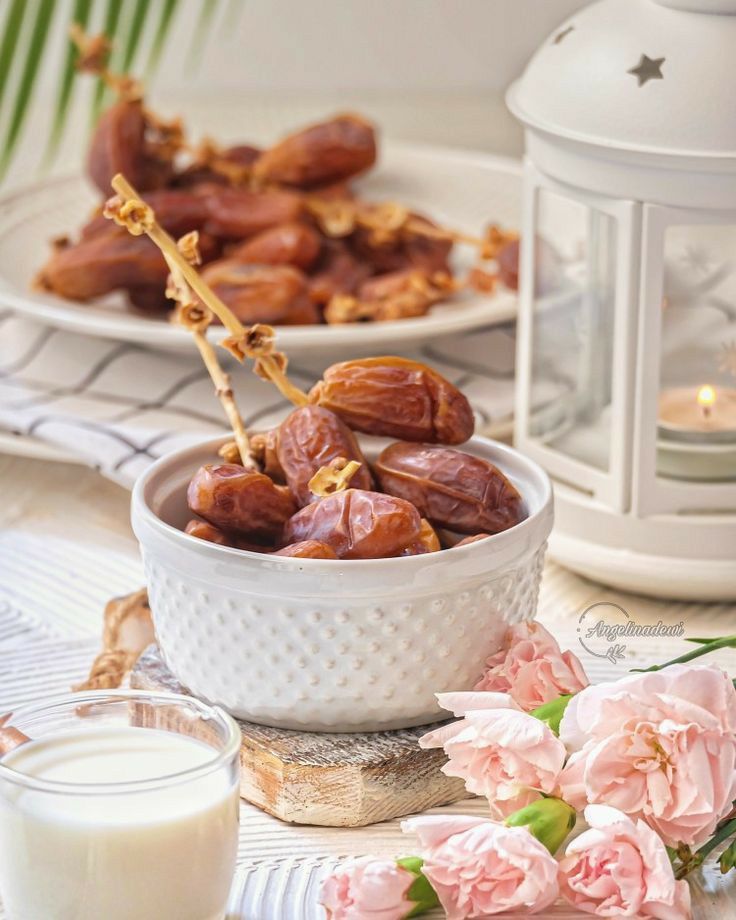 there is a bowl full of dates next to a glass of milk and some flowers