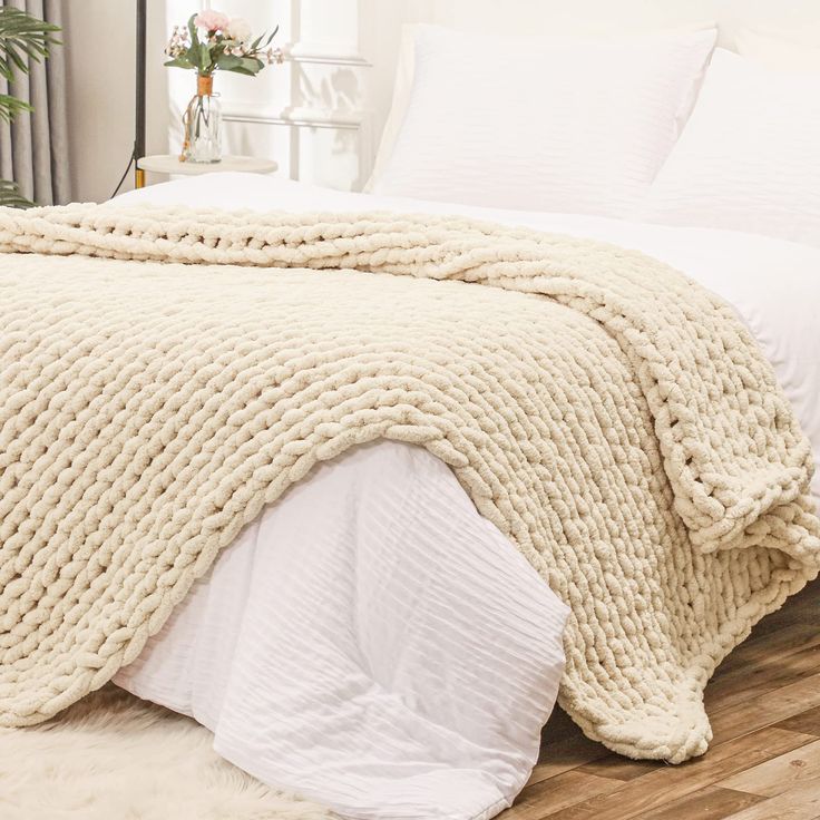 a large white blanket on top of a bed in a bedroom next to a plant