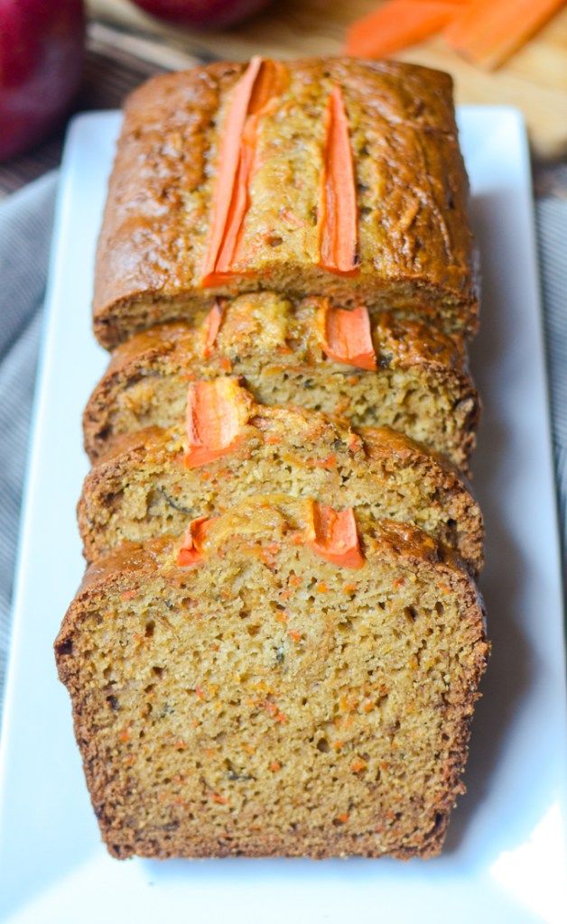 sliced loaf of carrot bread on a white plate with apples in the backgroud