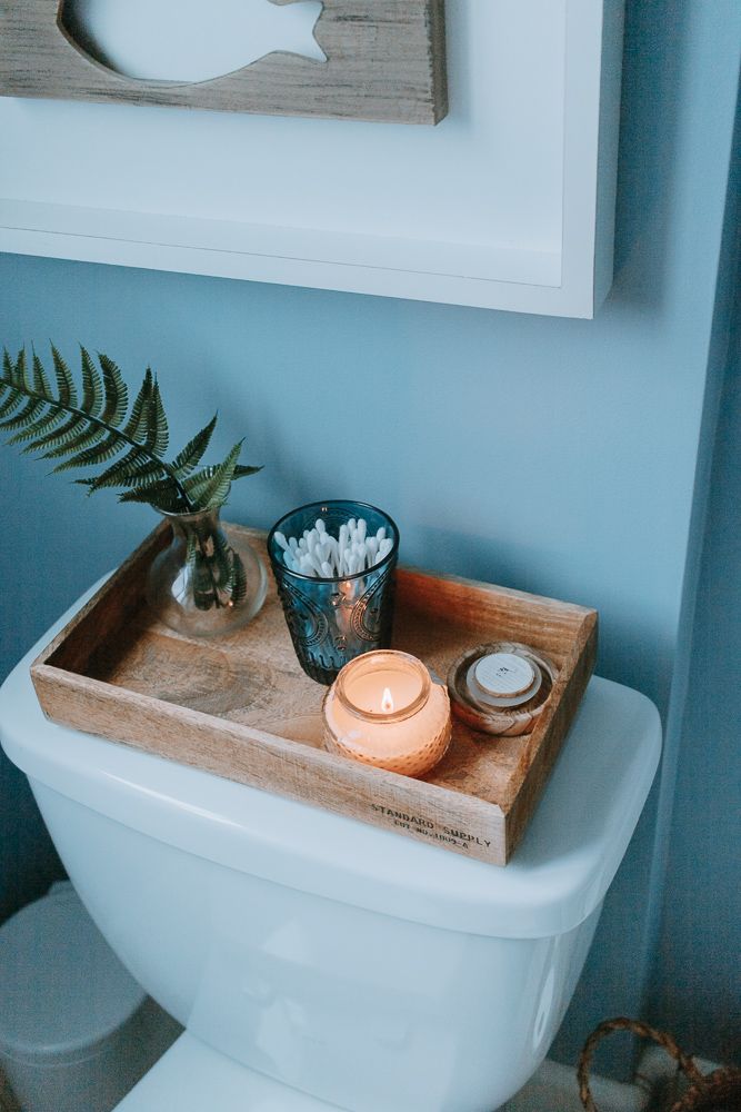 a white toilet sitting in a bathroom next to a wooden tray filled with flowers and candles