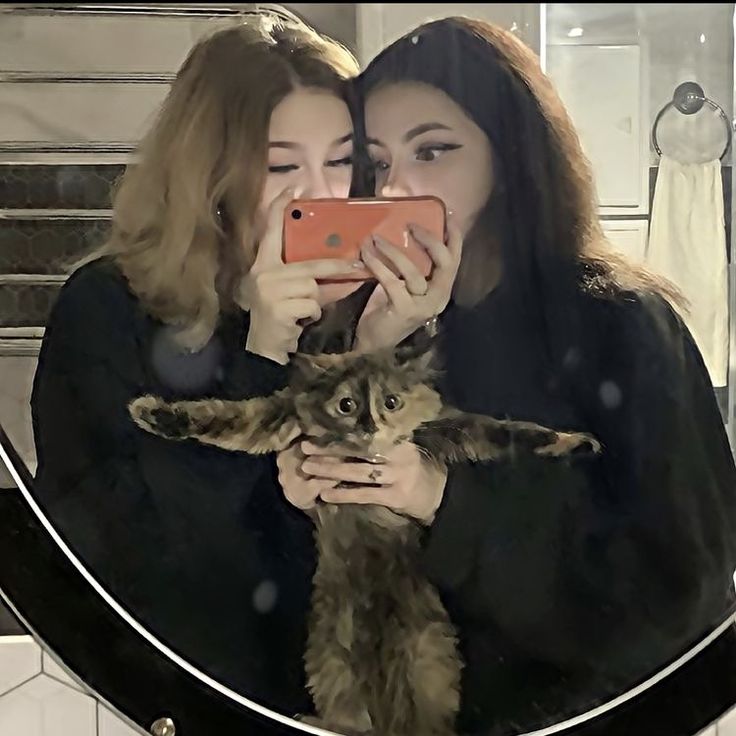 two women taking a selfie in front of a mirror with a cat on it