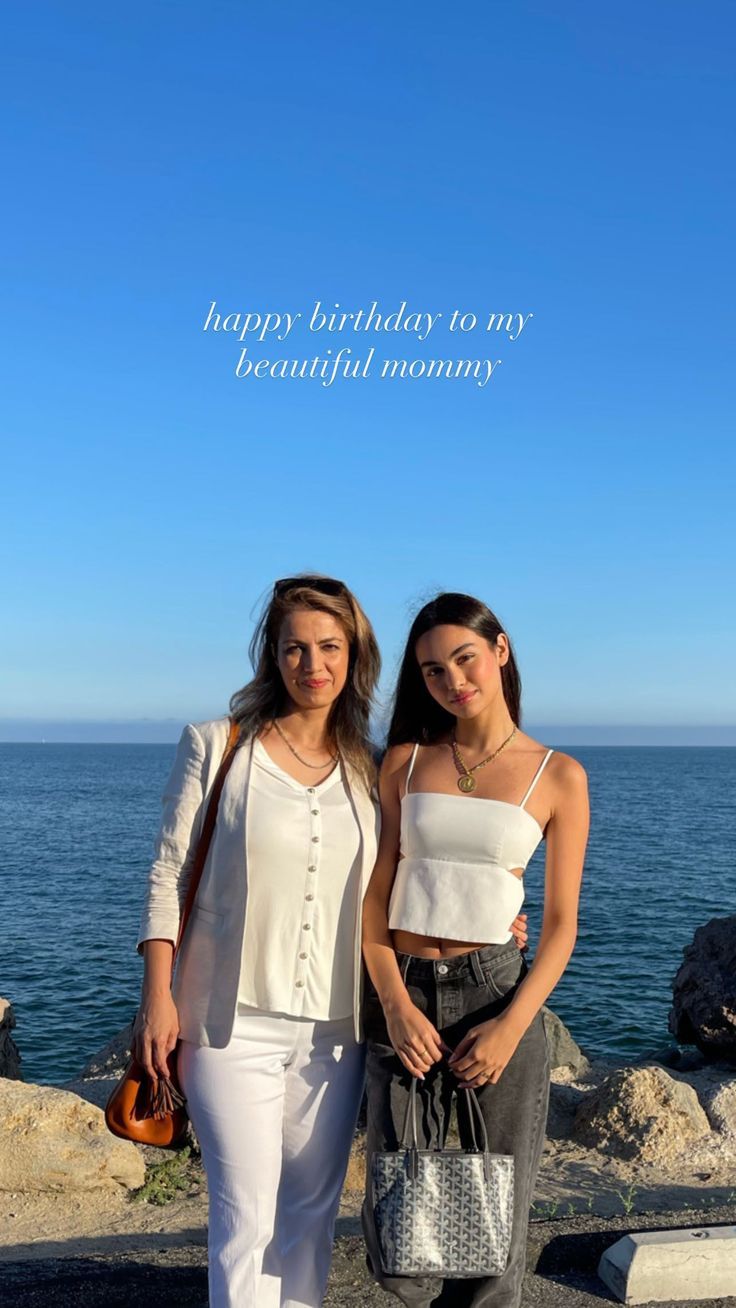 two women standing next to each other in front of the ocean with a happy birthday card