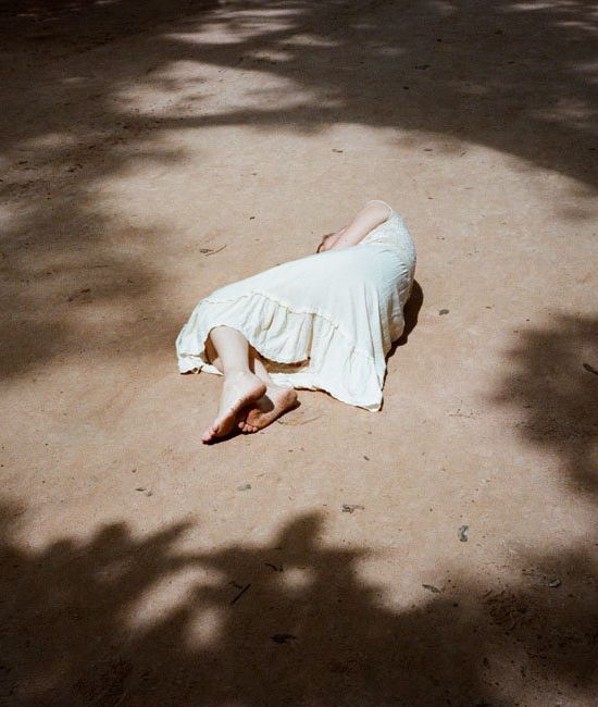 a woman laying on the ground in a white dress with her head down and hands behind her back