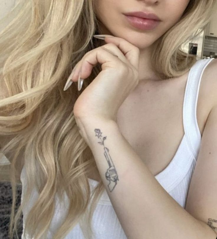 a woman with long blonde hair wearing a white tank top and tattoos on her arm