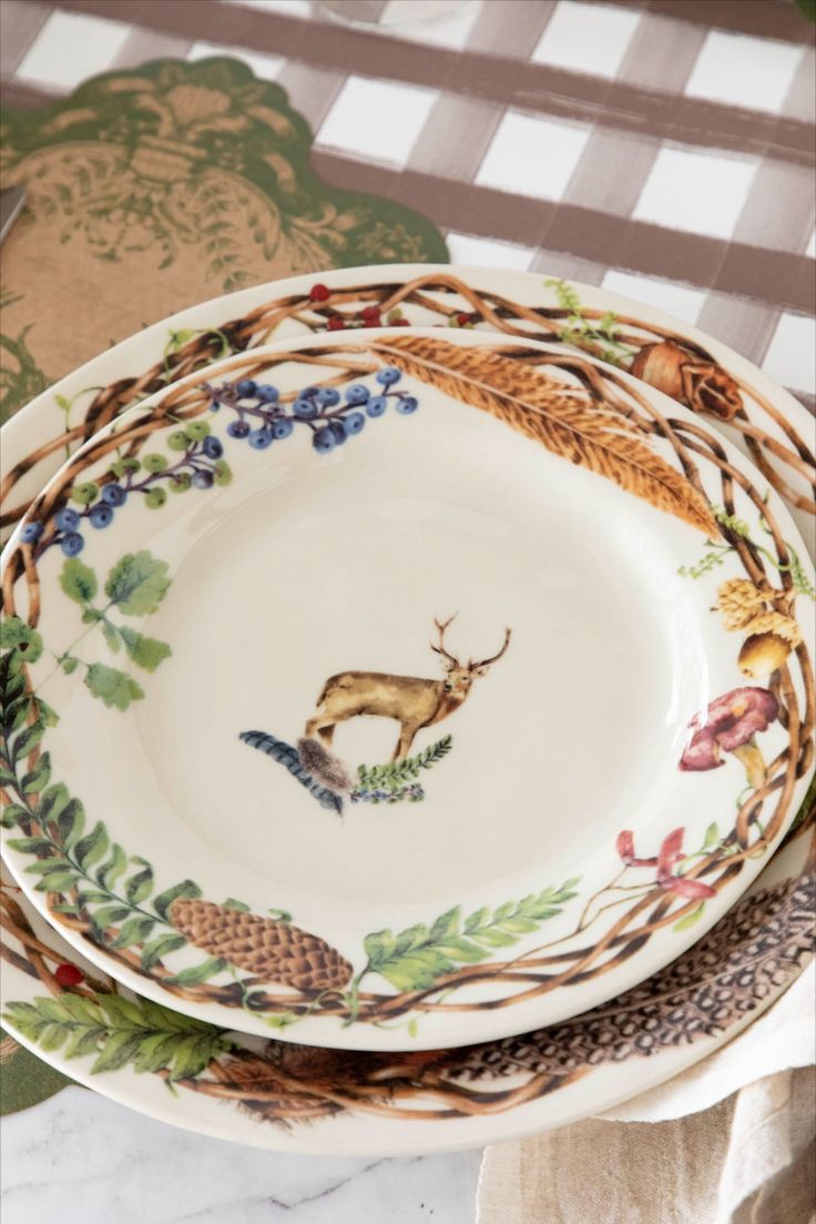 three plates are stacked on top of each other with deer and pine cones painted on them