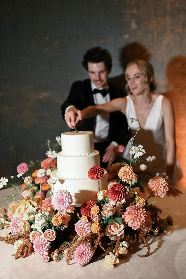 a bride and groom are cutting their wedding cake with flowers on the table in front of them