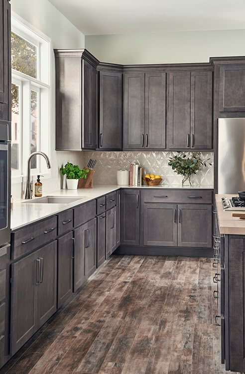 a kitchen with dark gray cabinets and white counter tops, wood flooring and large windows