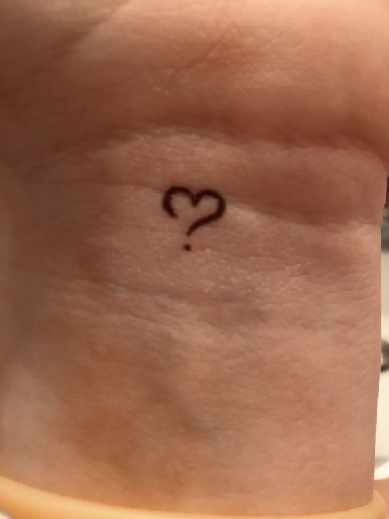 a small heart tattoo on the back of a woman's left arm and wrist