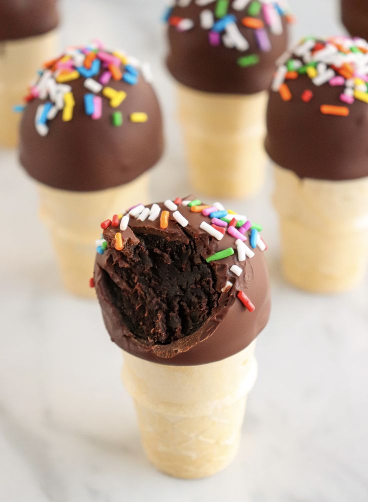 ice cream cones with chocolate frosting and sprinkles in them on a marble surface