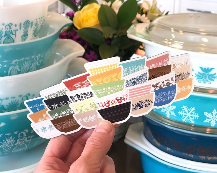 a person holding up some stickers in front of many bowls and plates with flowers on them