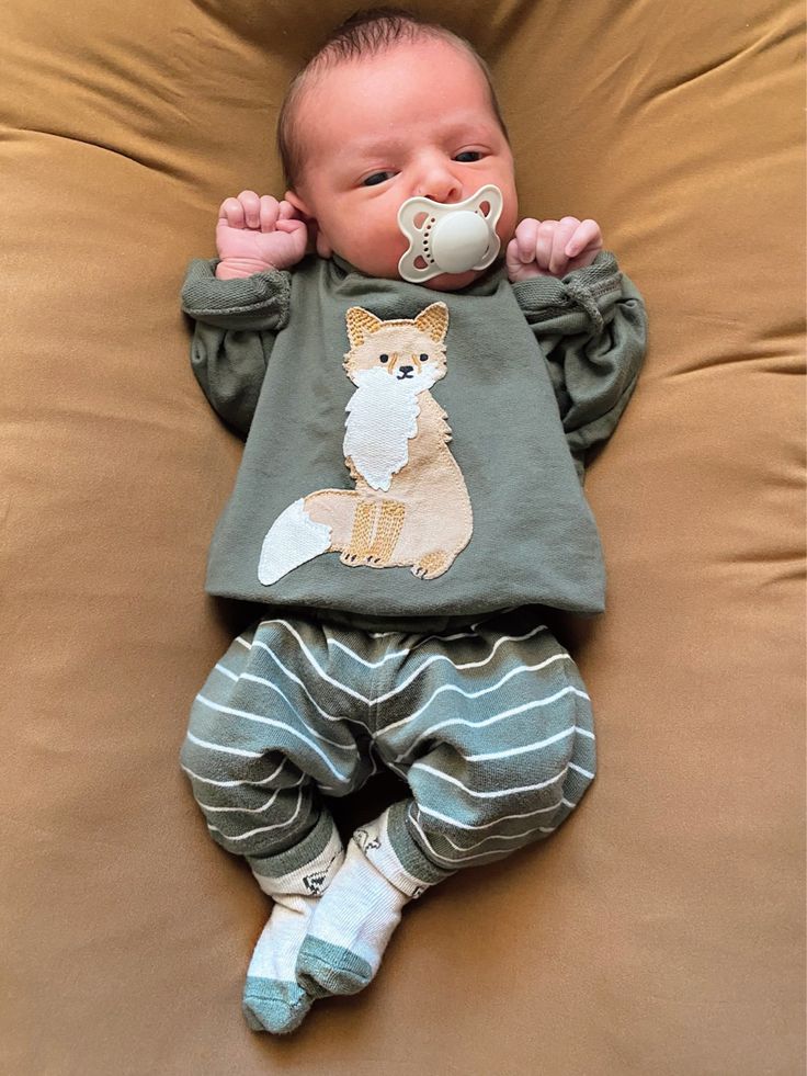 a baby with a pacifier in its mouth is laying on a brown couch and wearing pajamas