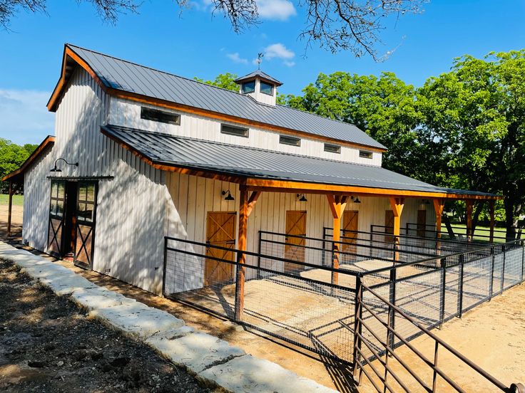 a horse barn with a metal roof and two stalls on each side, surrounded by trees